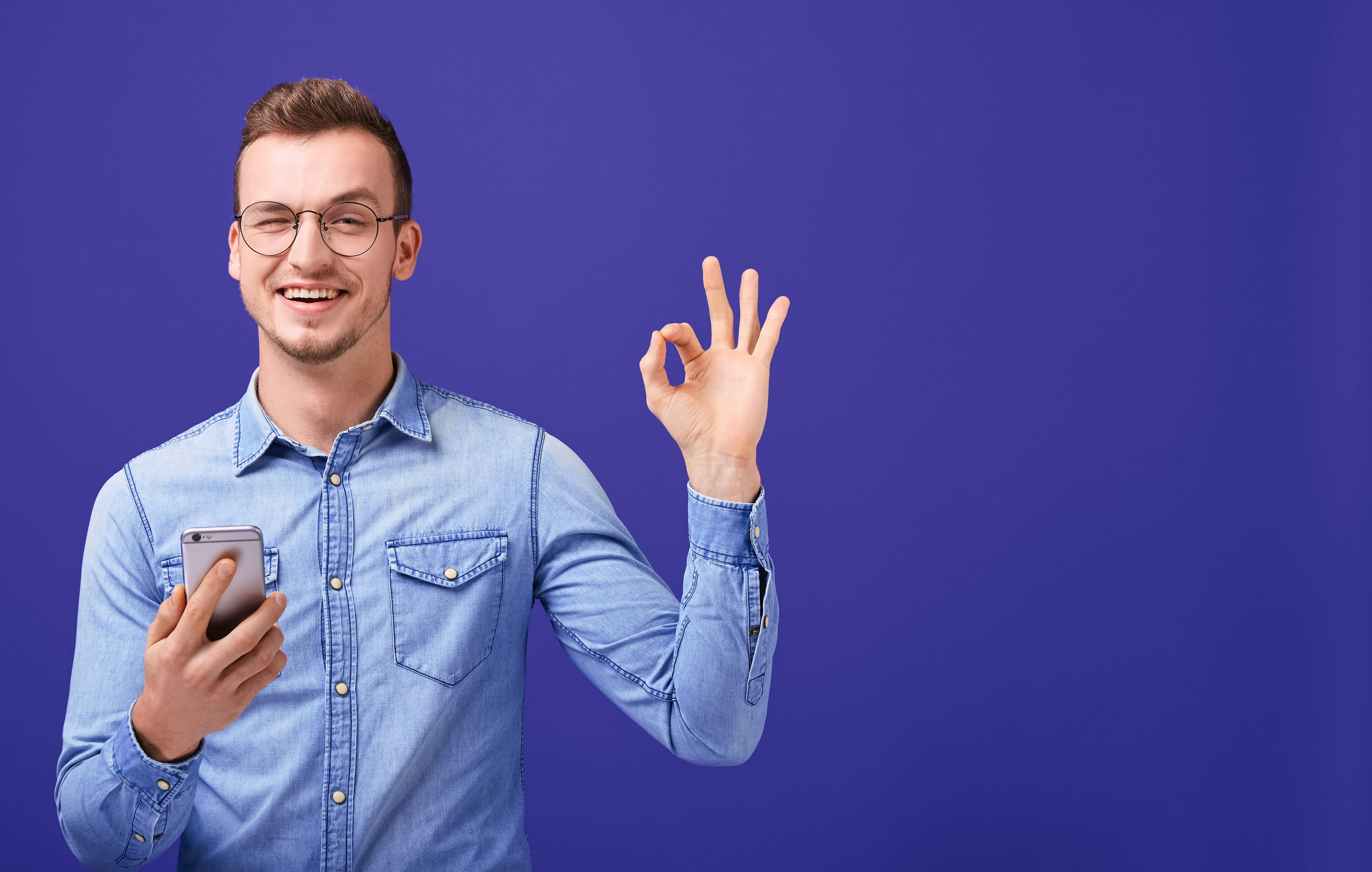 Fotografía: hombre con celular en la mano, y con la otra haciendo gesto de OK